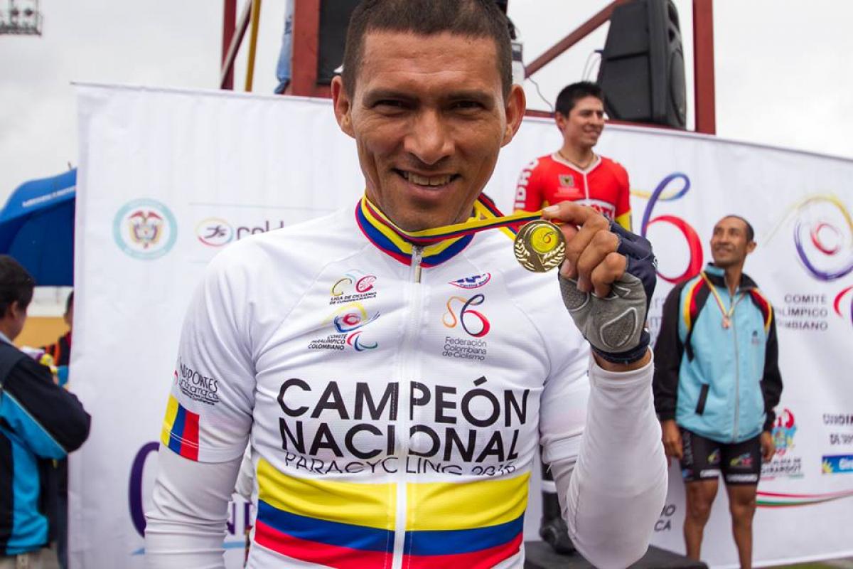 Man with cycling jersey showing his medal, smiling