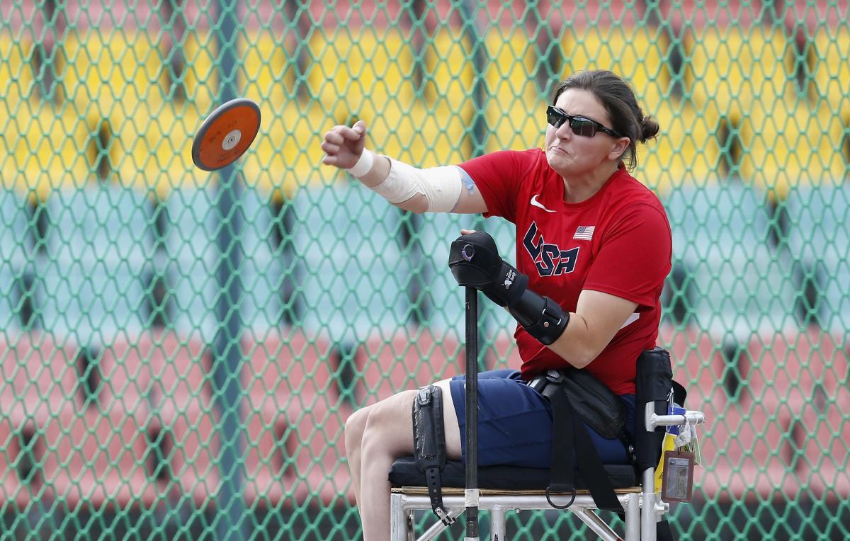 Woman sits in chair and throws discus