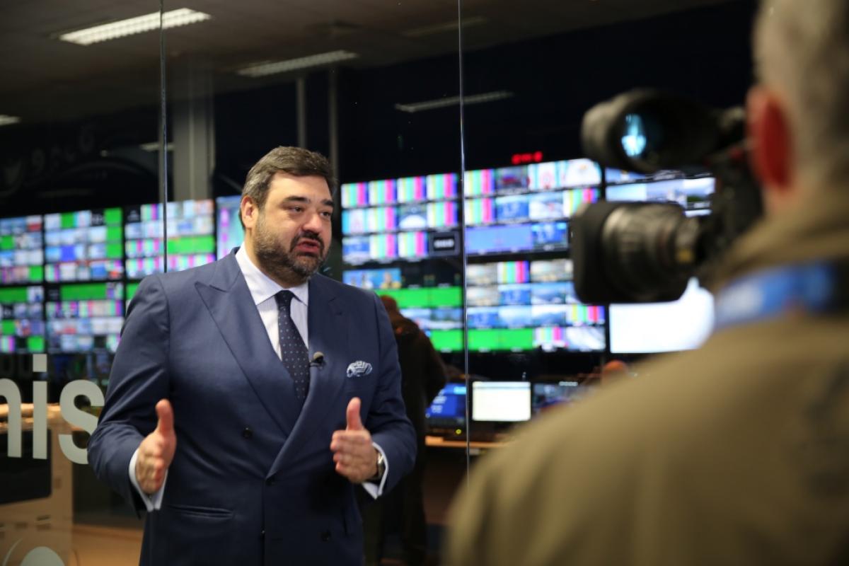 Man in suit being filmed in front of many monitors