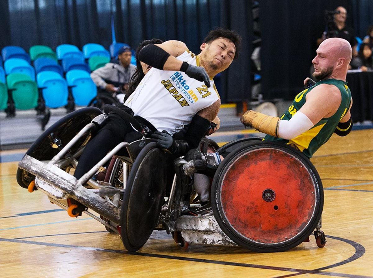 Two men playing wheelchair rugby collide their chairs.