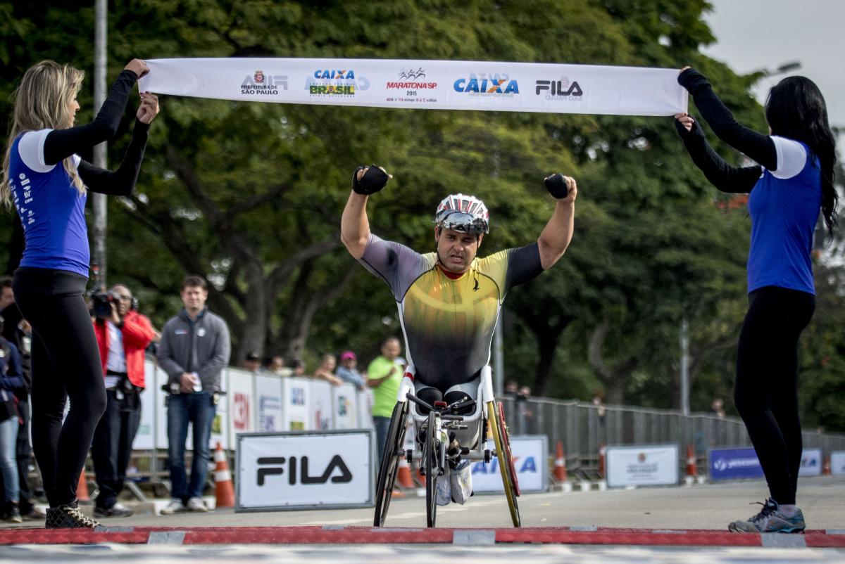 Brazil's Fernando Aranha Rocha - triathlon Man in wheelchair raises both arms as he crosses a finishline.