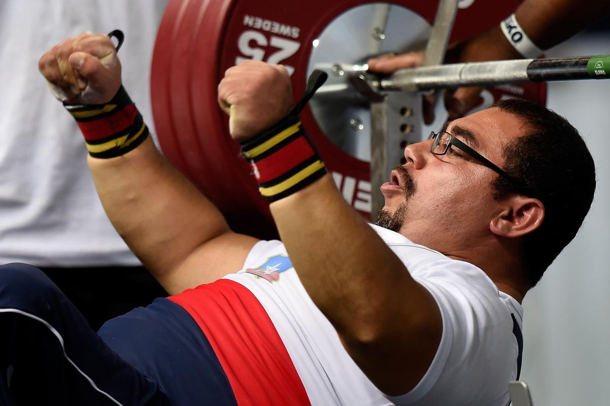 Chilean powerlifter Juan Carlos Garrido is on the bench and raises his hands celebrating his win.