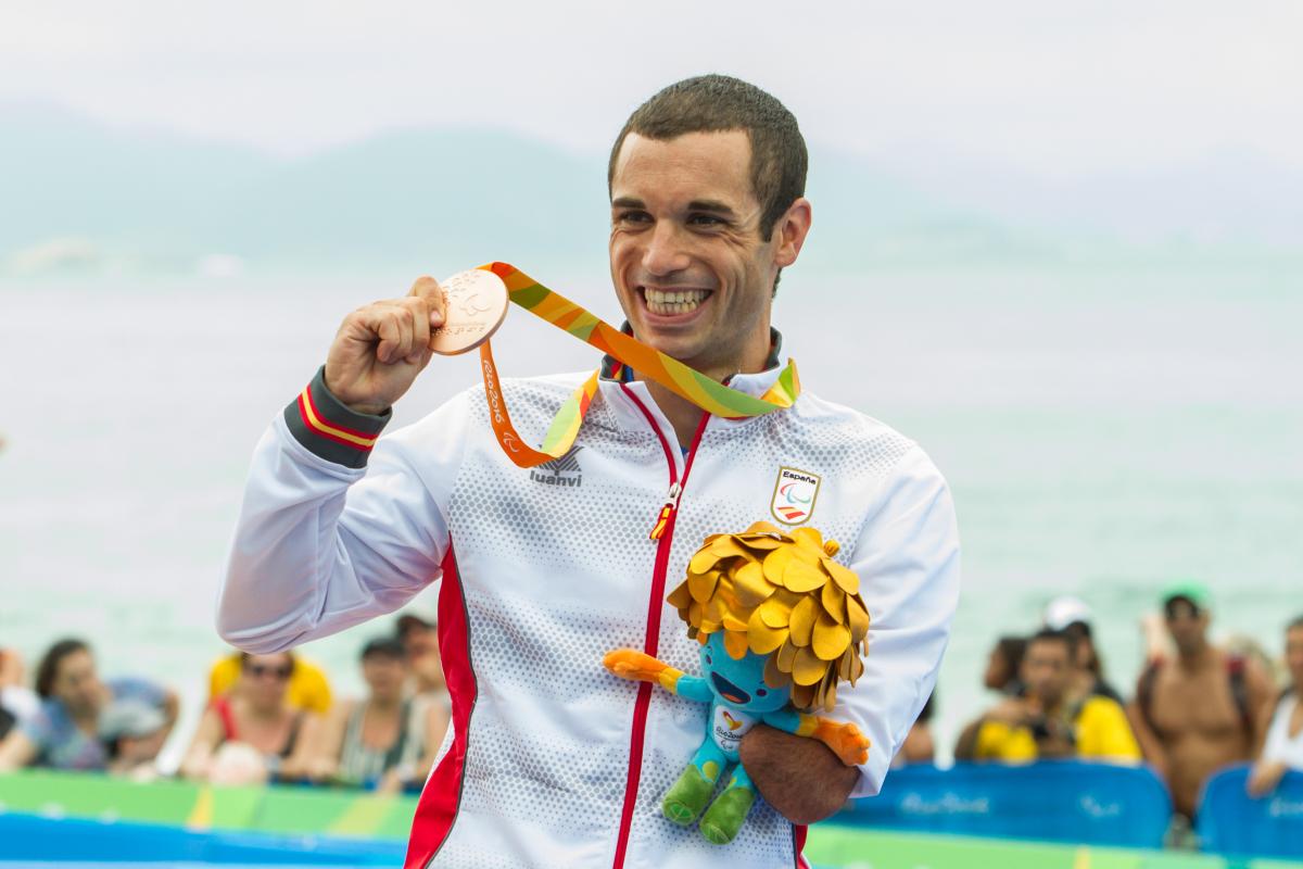 Triathlon Men - PT4 Victory Ceremony - Rio 2016 man stands on podium holding up a medal and a mascot