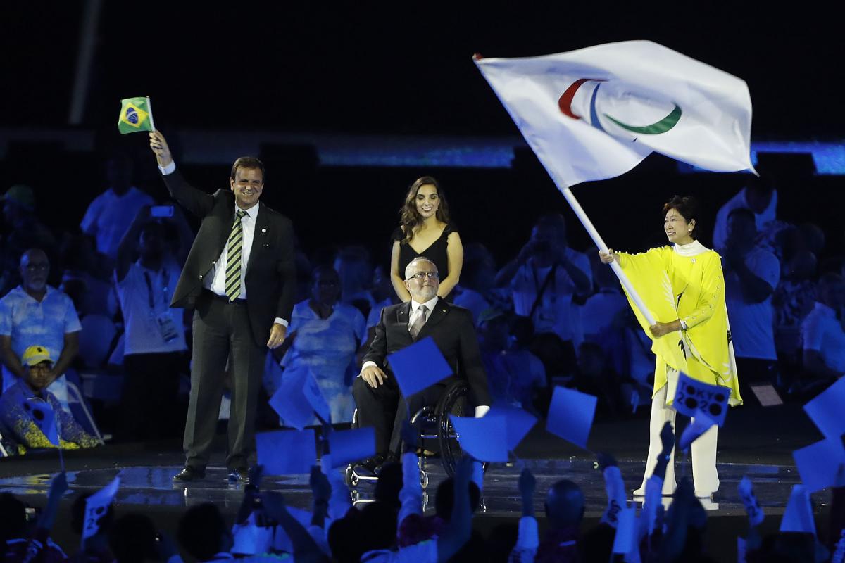 Three people on a stage, one woman waving a flag