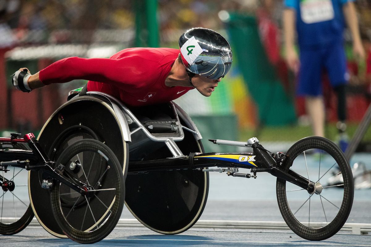 Close up of a wheelchair racer with a red racing suit and a silver helmet.