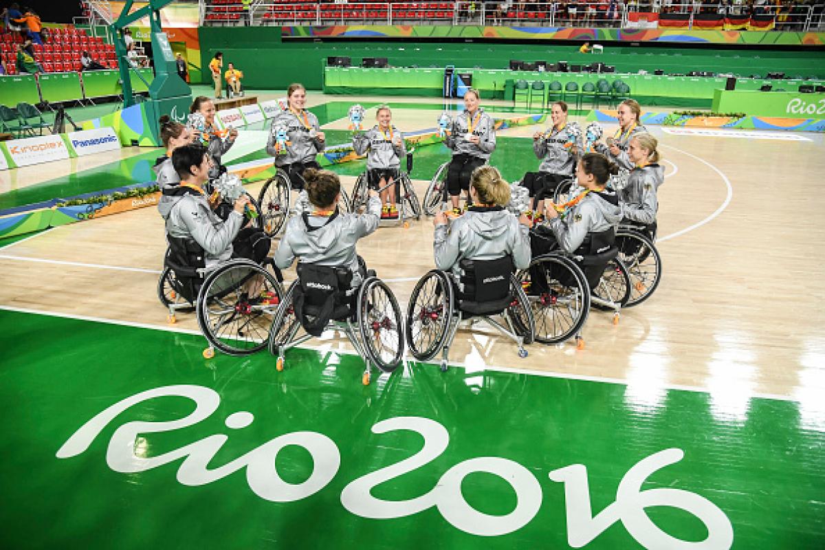Women in wheelchairs forming a circle on a basketball field