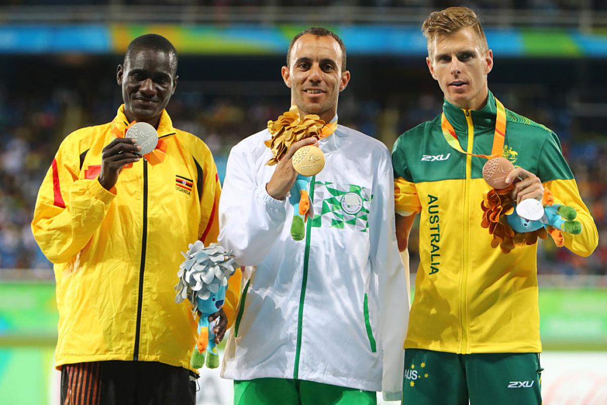 Uganda's track and field athlete David Emong celebrates on the podium with the gold and bronze medallists.