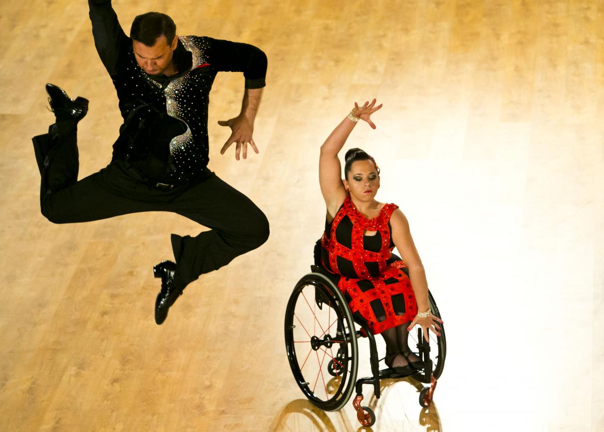 A woman in wheelchair dances with her stand-up partner who is jumping