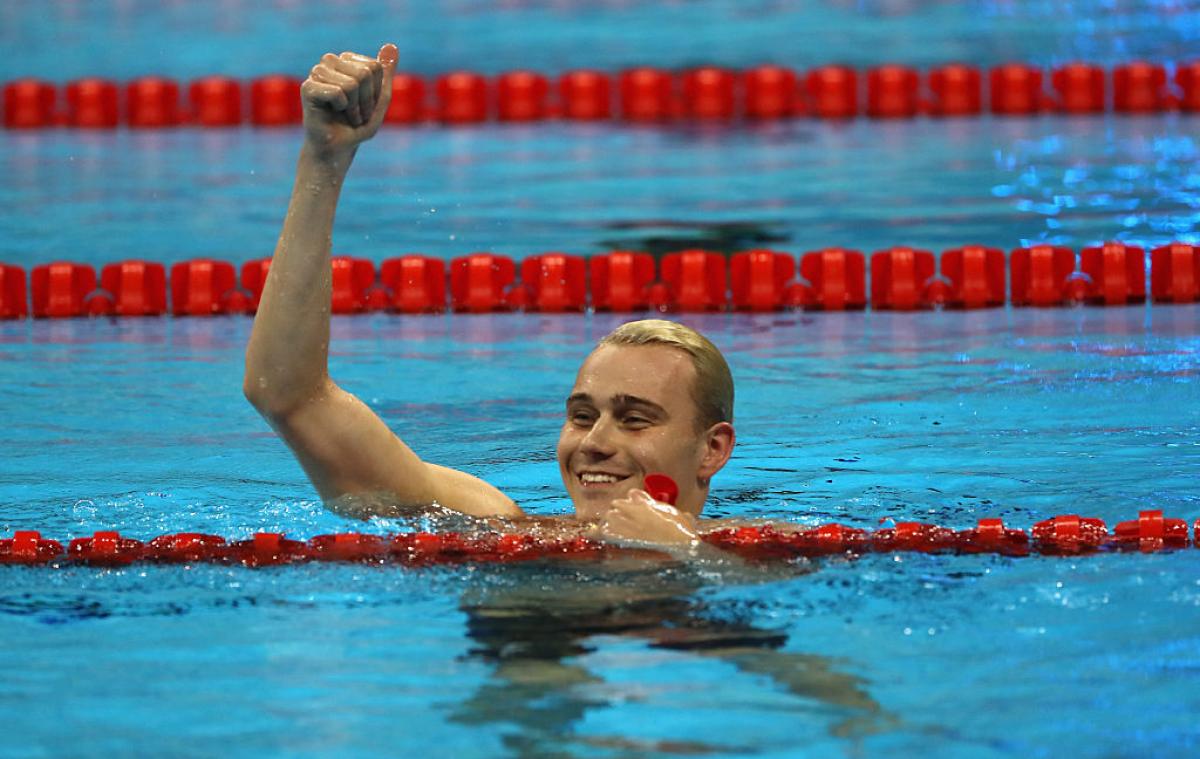 A swimmer celebrating his gold medal in the water, raising one arm.