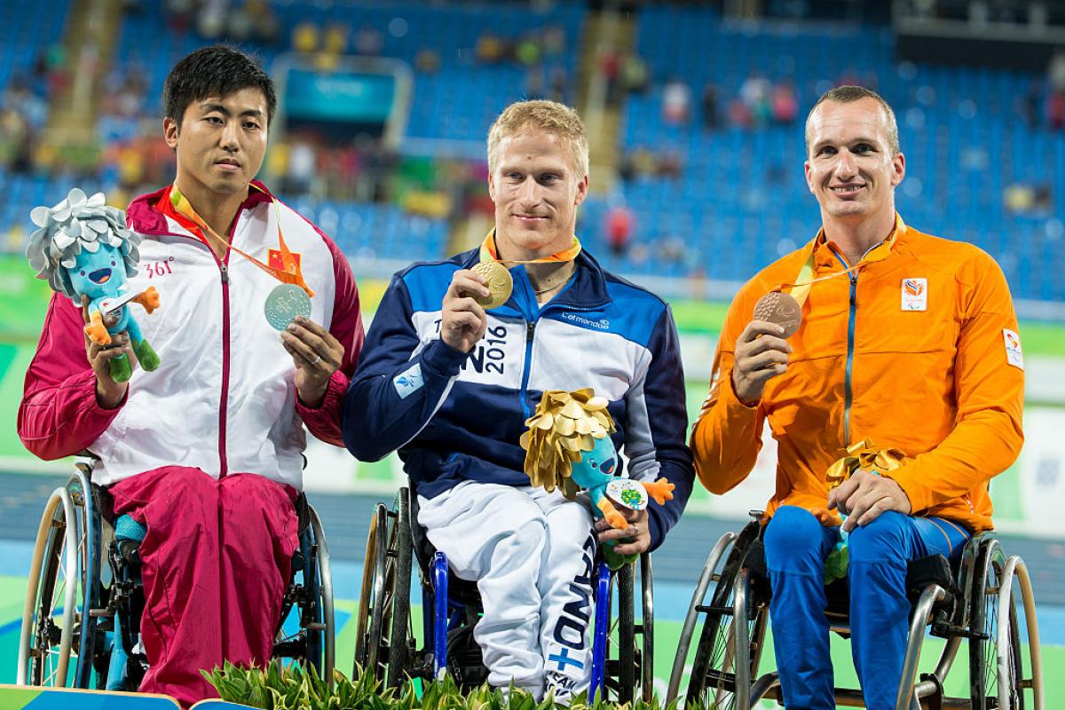 Three men in wheelchairs on a podium showing their medals
