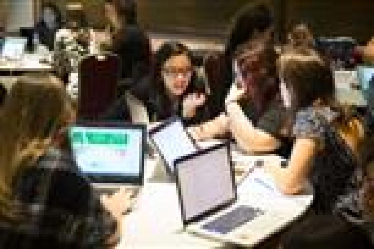 Group of young people sitting around a table with laptops, discussing