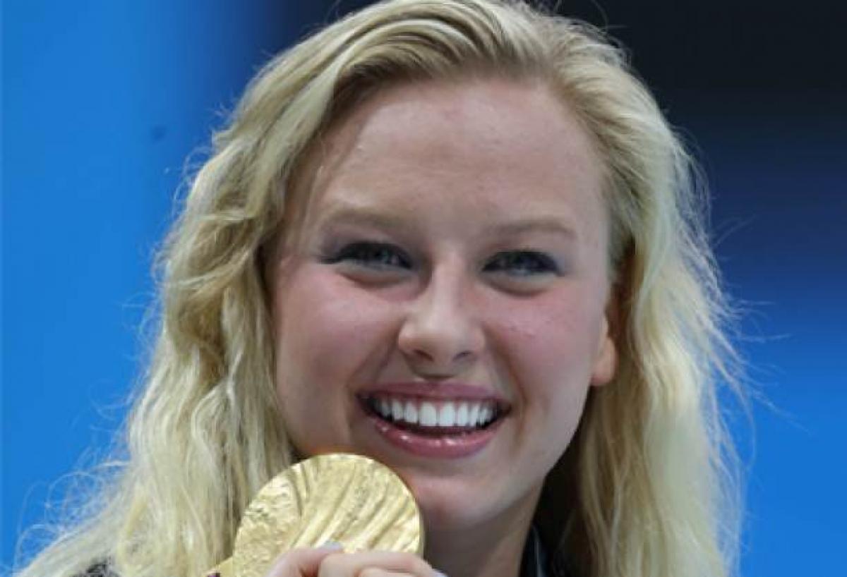 A portrait of a blond woman showing her gold medal