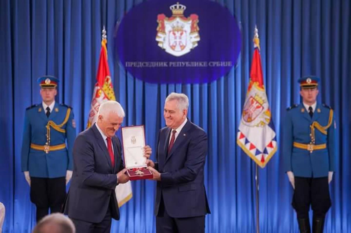 Two men on a stage, one handing a medal to the other