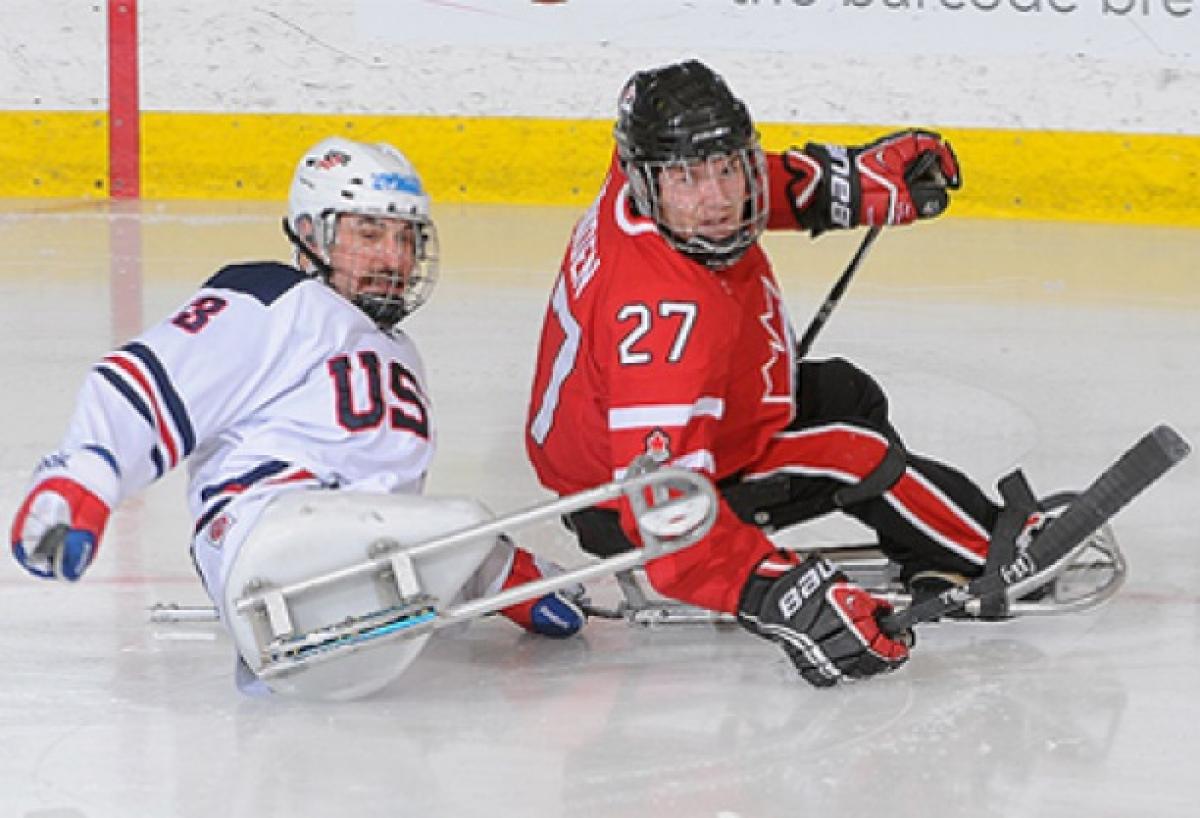 A picture of two men in sledges playing ice hockey