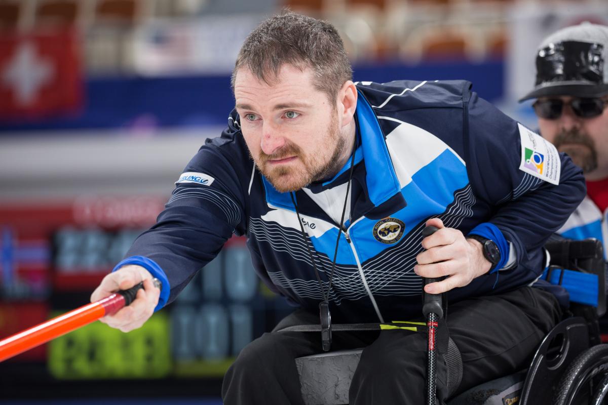 Man in blue training suit and in wheelchair focusing on something behind the camera