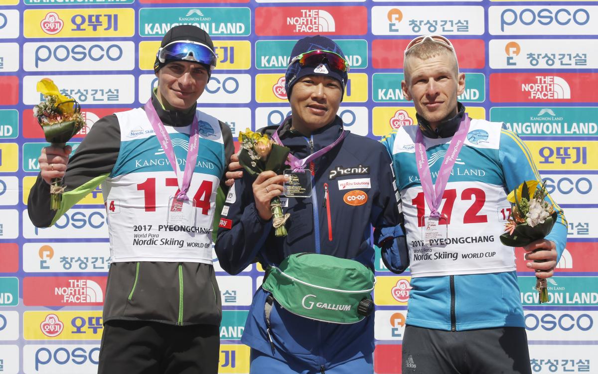 Three men on a podium, holding flower bouquets