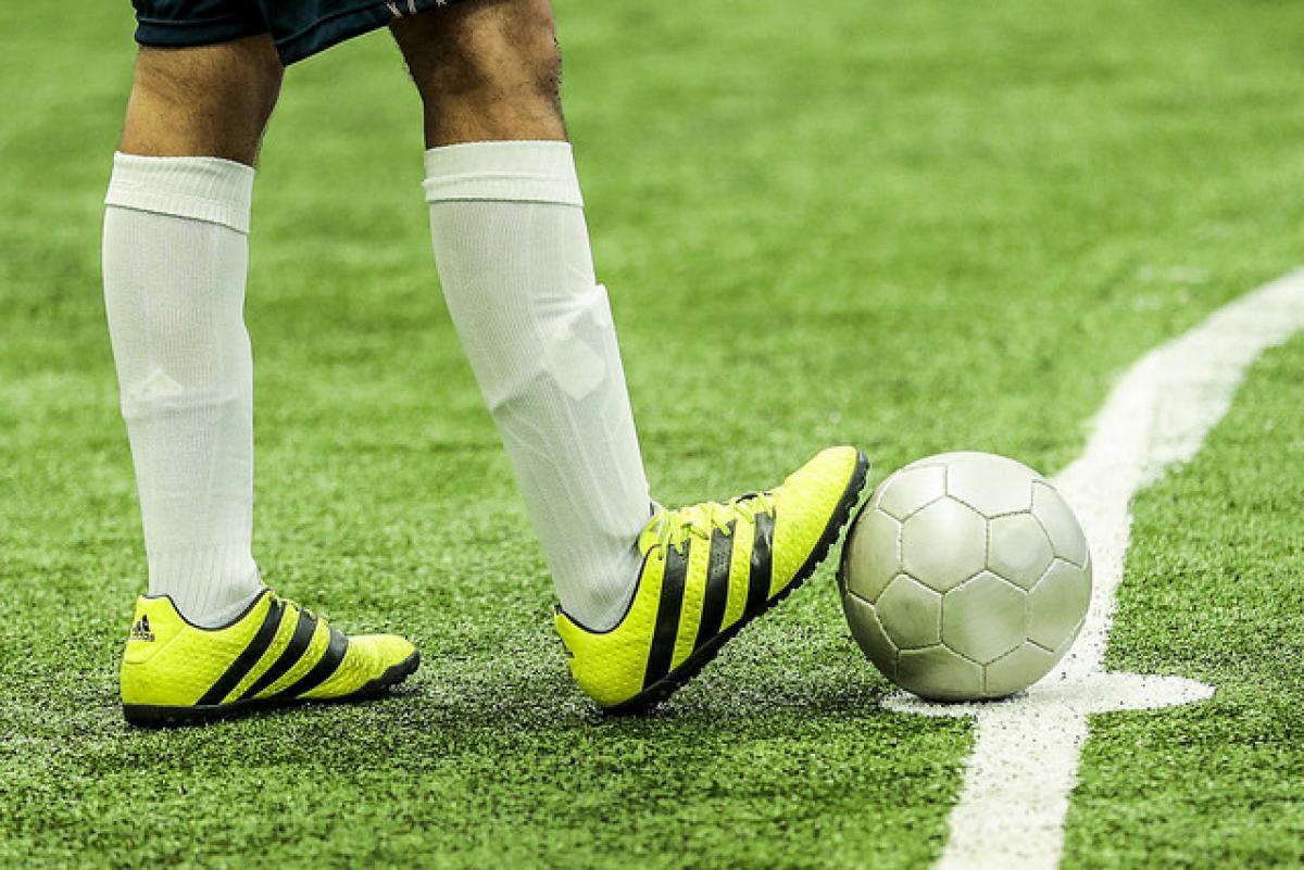 A man withbright yellow football boots rests his foot on a ball.