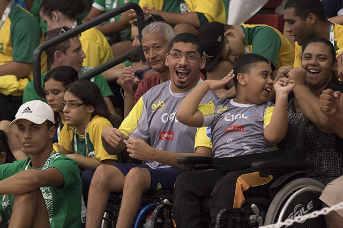 A man and a boy in a wheelchair watch a wheelchair basketball competition