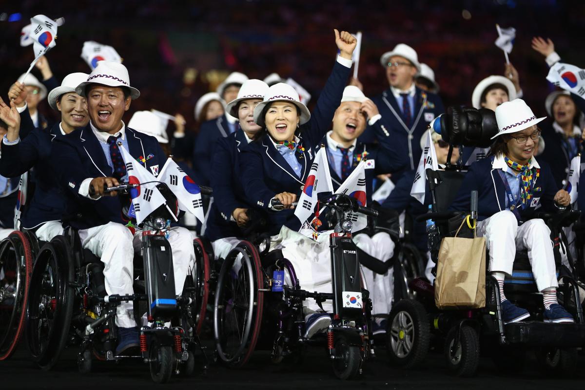 South Korean athletes in wheelchairs hold flags as they enter the stadium