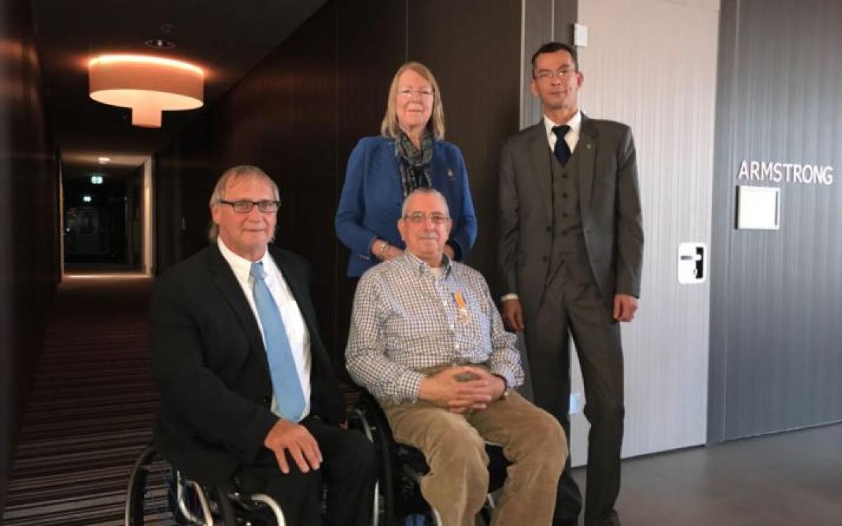 IWBF Ron Coppenrath - wheelchair basketball Two men in wheelchairs in suits while two people stand behind them to pose for a photo