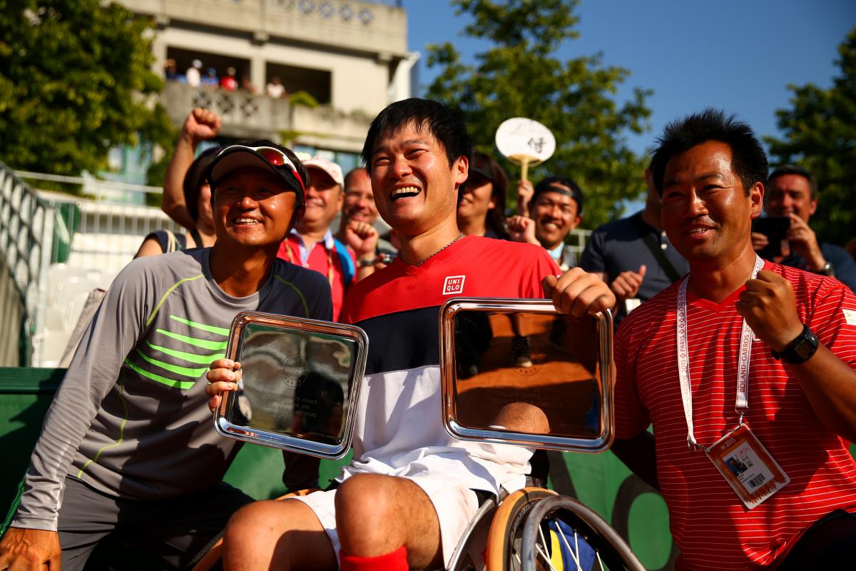 Japan's Shingo Kunieda - wheelchair tennis Man in wheelchair holds trophies with two other men next him.