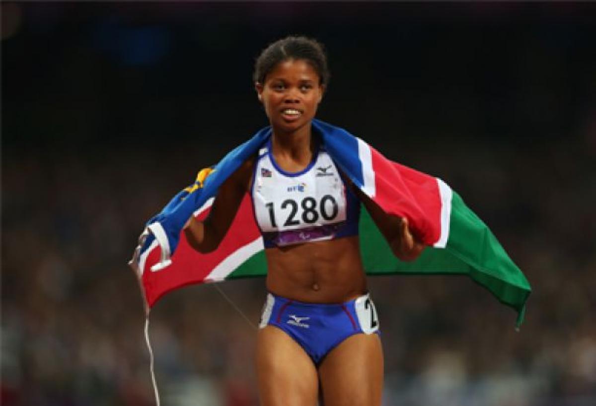 A picture of a woman running with a Namibian flag on her shoulder 