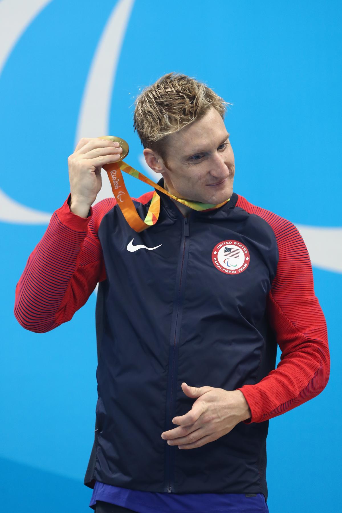 Blind man on podium shakes his gold medal near his ear