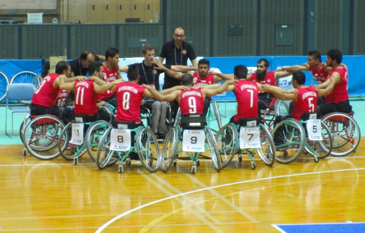Men in basketball wheelchairs huddle around each other