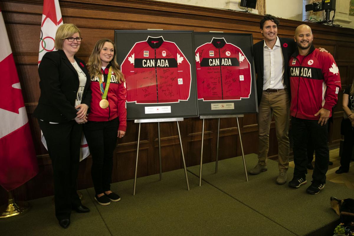 Four people stand between two signed jerseys, posing for a photo