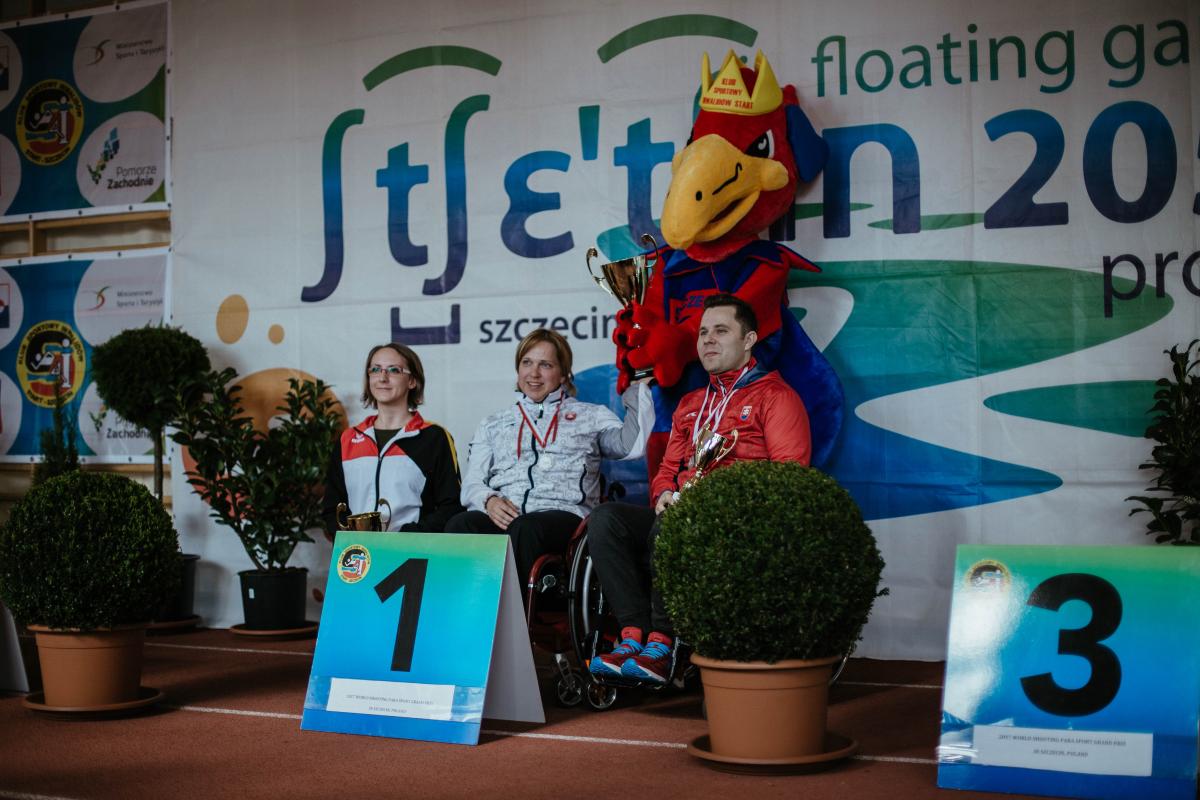 Shooting - Veronika Vadovicova, Natascha Hiltrop, Radoslav Malenovsky Three shooters on a podium with event mascot