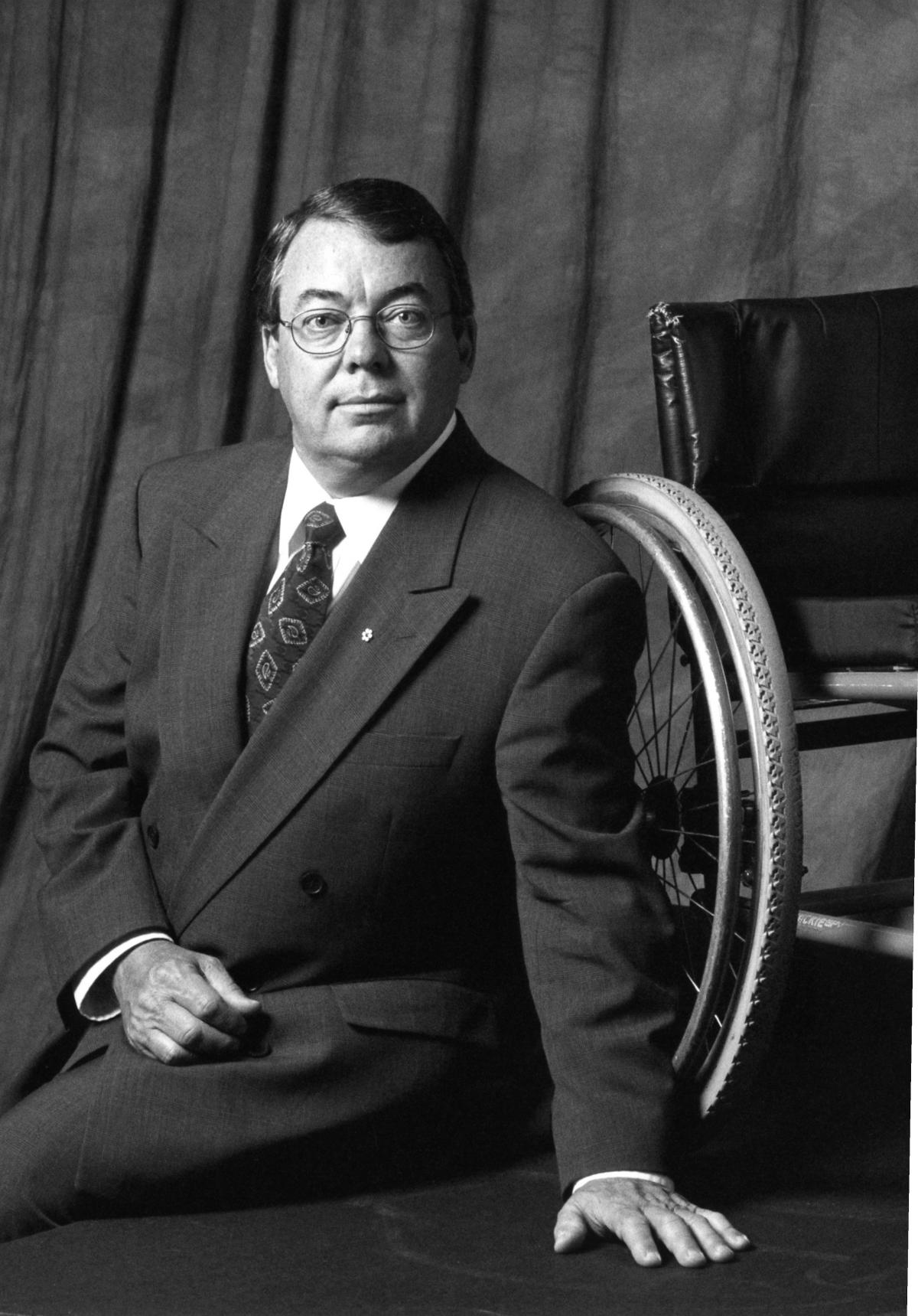 Black and white portrait of a man sitting infront of a wheelchair 