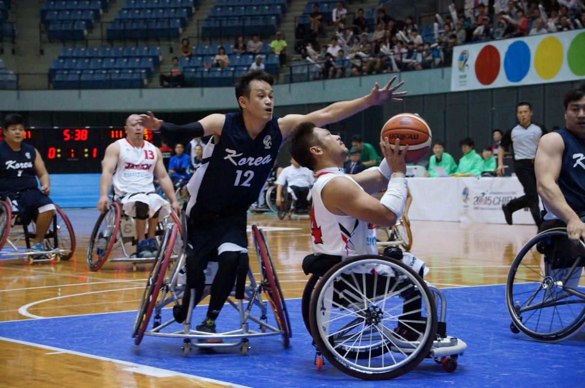 Man in wheelchair tries to block another man in wheelchair playing basketball