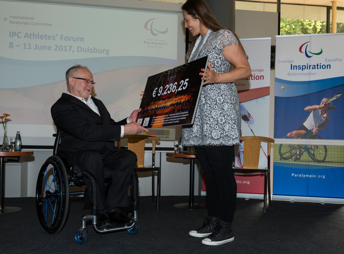 IPC Athletes' Forum - Elvira Stinissen and Sir Philip cheque Woman presents man in wheelchair with a cheque