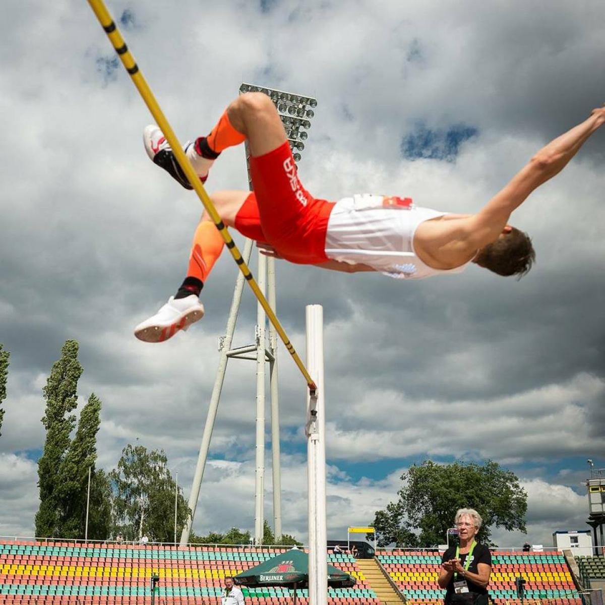man jumps horizontally over high jump bar