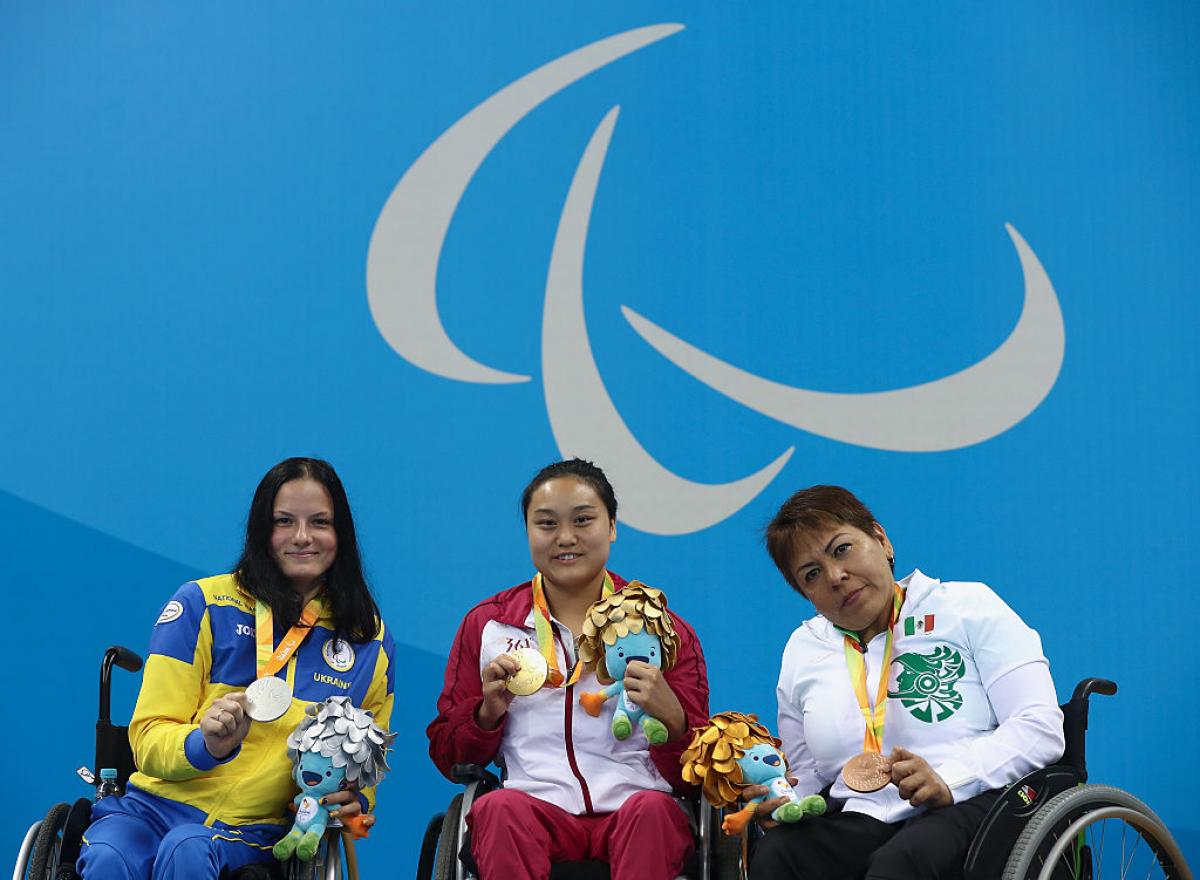 three women in wheelchairs holding medals on a podium