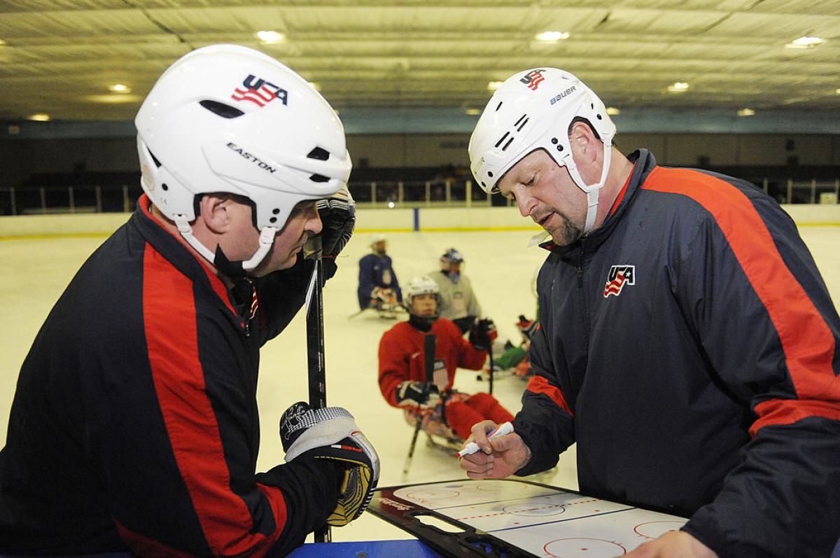 two men discuss ice hockey tactics on a tactics board