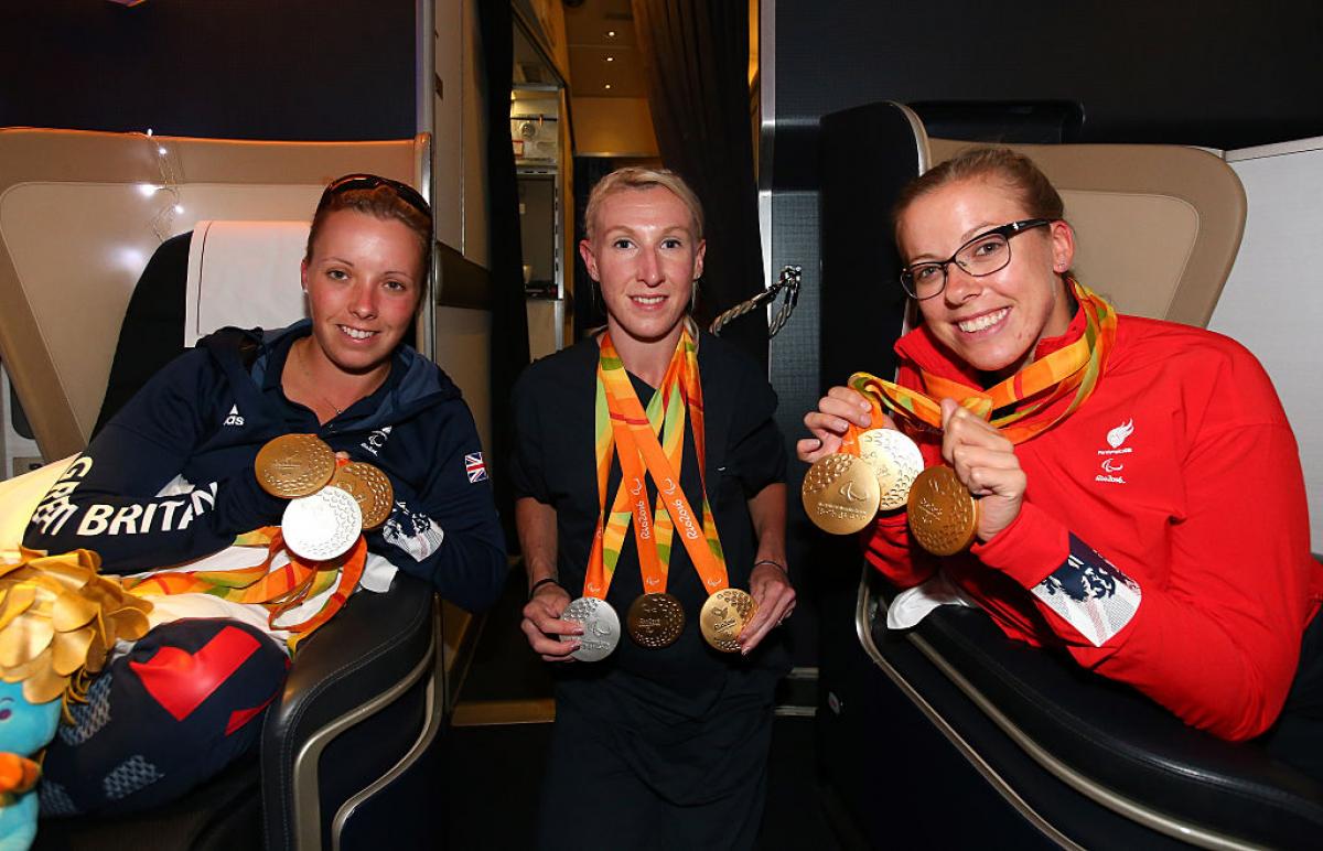 three women on a plane holding their Paralympic medals and smiling