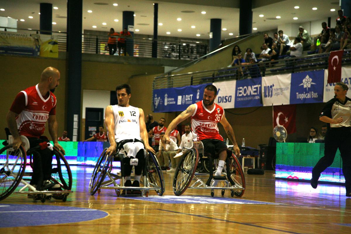 a group of men in wheelchairs challenge for a basketball