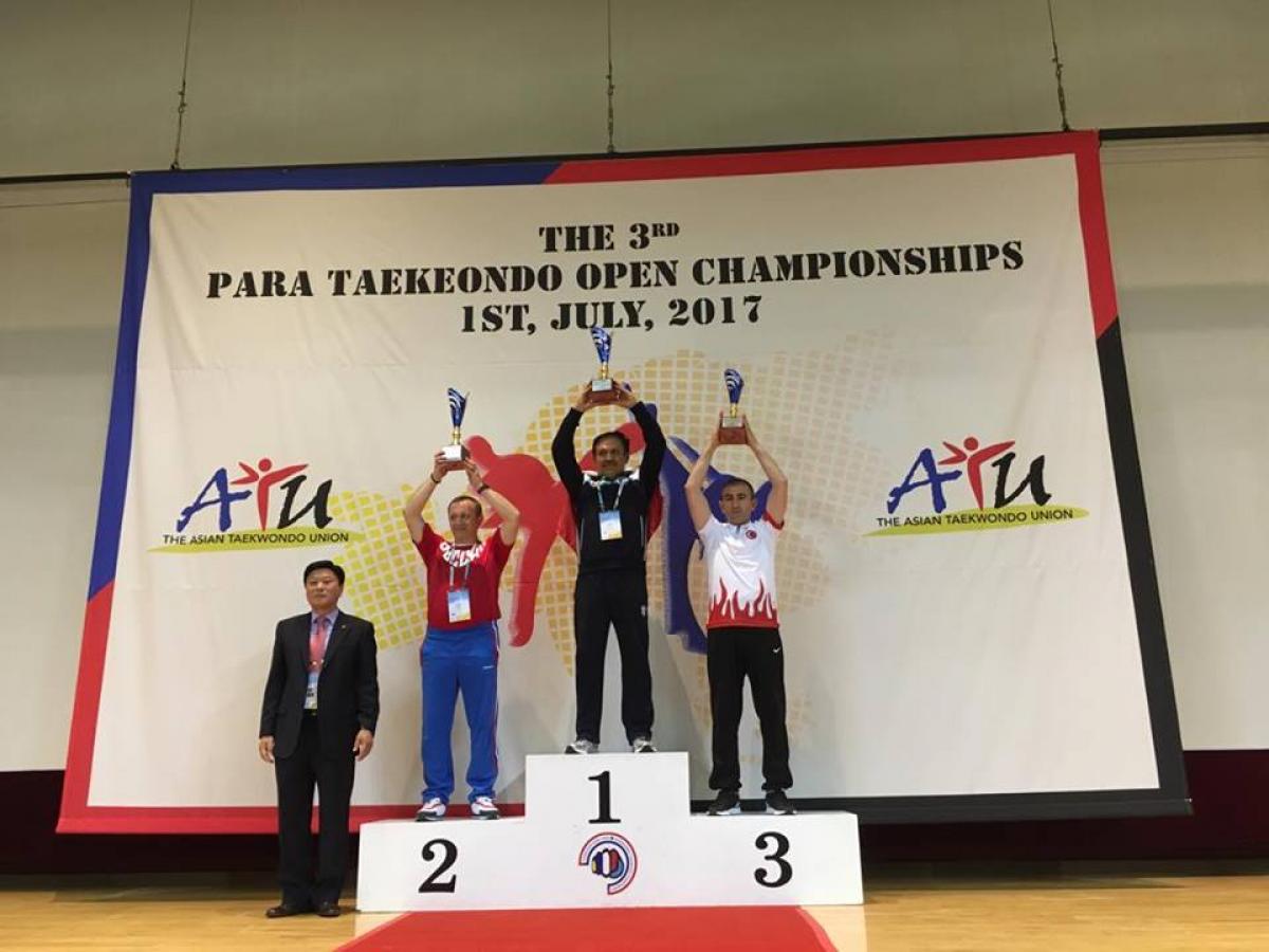 three men hold trophies on a podium