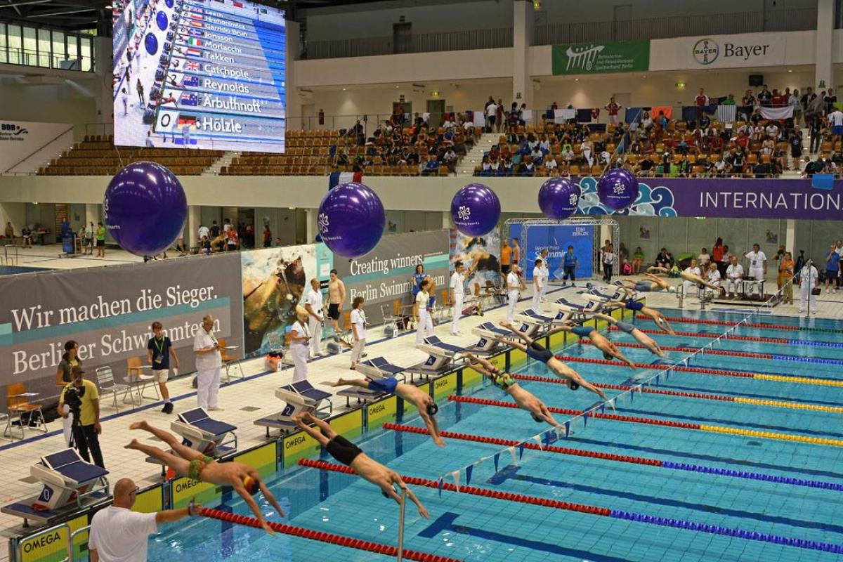 a group of male para swimmers dive into the pool