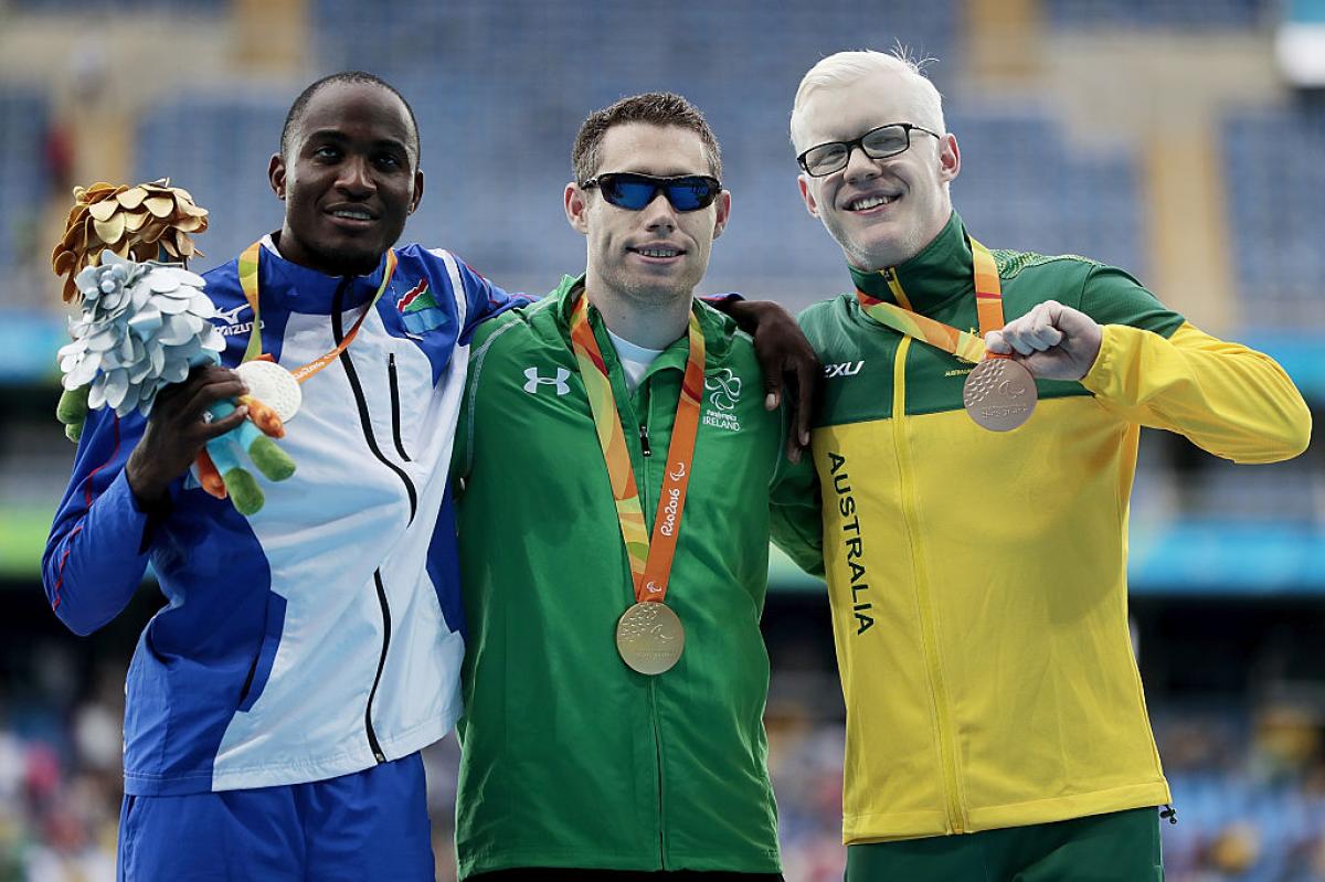 three men stand on a podium with their medals