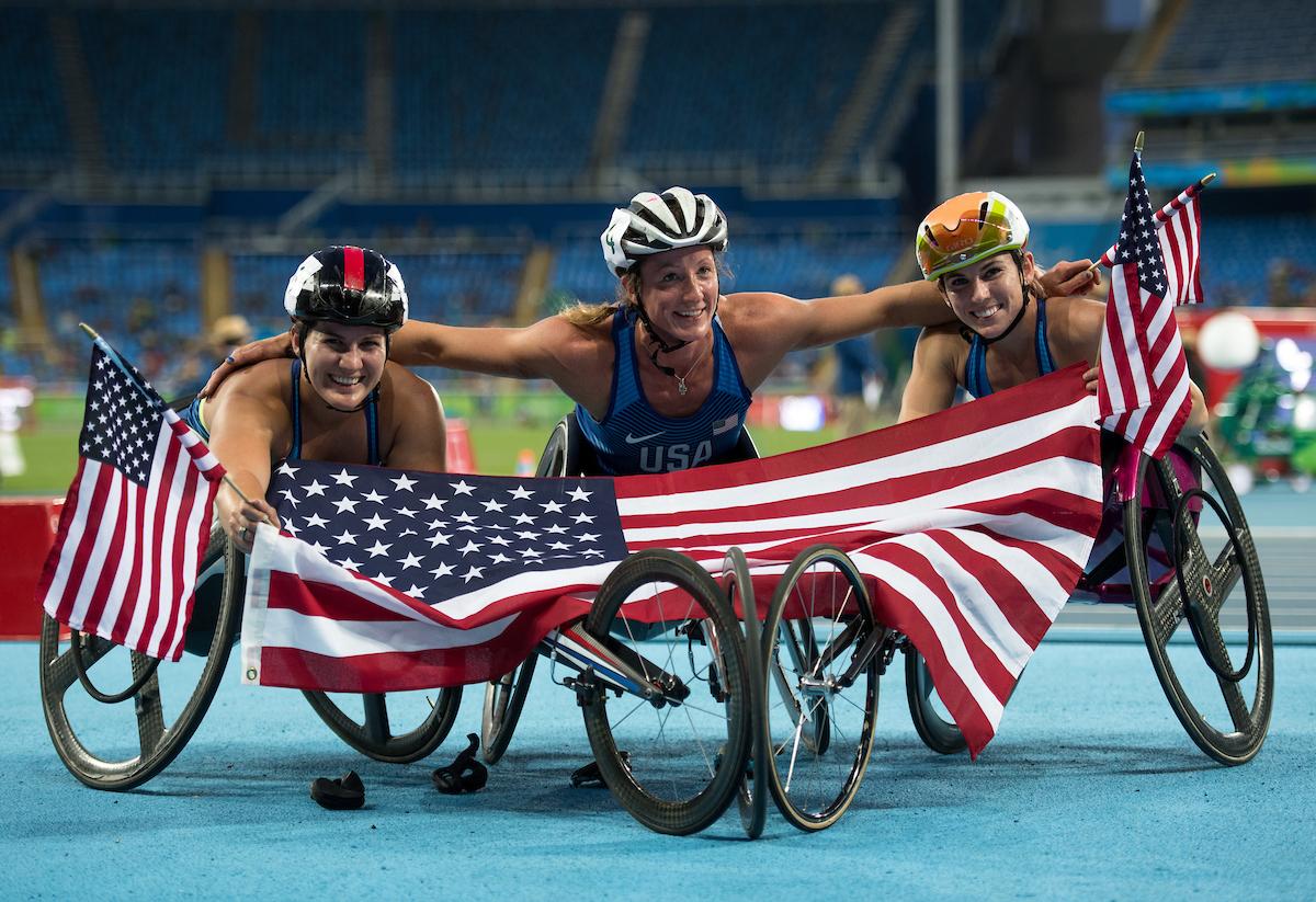 three female wheelchair athletes hold up the American flag