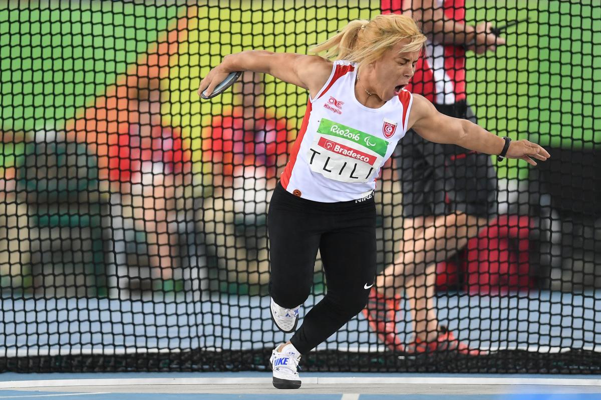 Raoua Tlili A woman in white vest and black bottoms pulls a face as she gets ready to throw a discus.