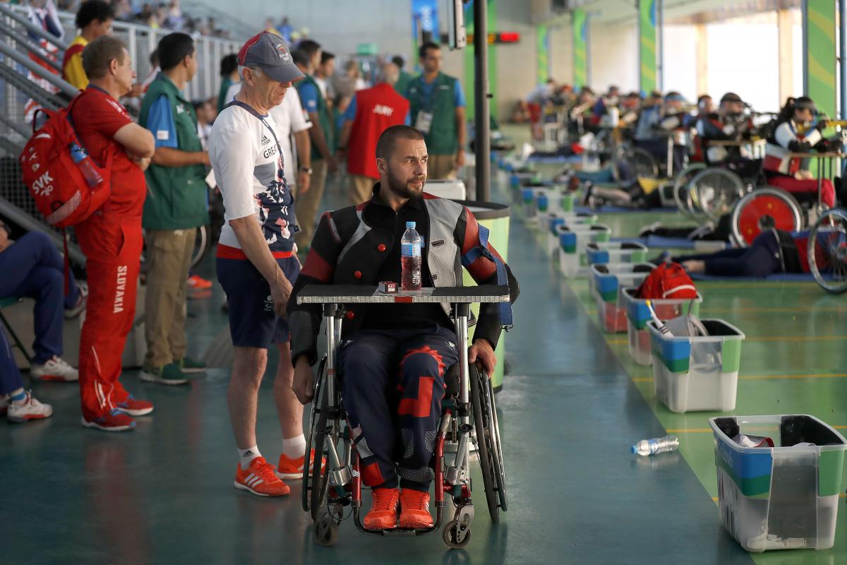 a para shooter in a wheelchair waits with his coach