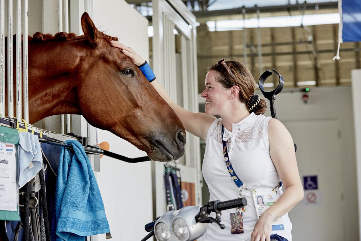 Sanne Voets a para equestrian rider pats her horse in the stables