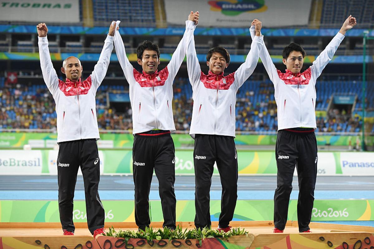 a group of four male Para athletes raise their arms in celebration