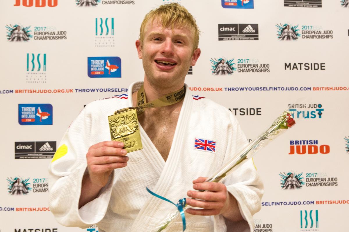 a man holds up his gold medal and smiles