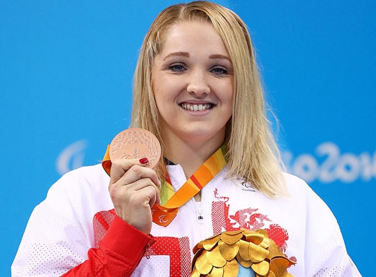 a woman holds up her medal and her mascot