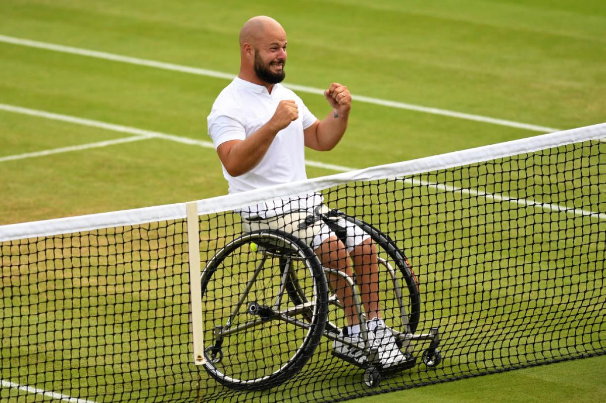 a wheelchair tennis player clenches his fists in celebration at the net