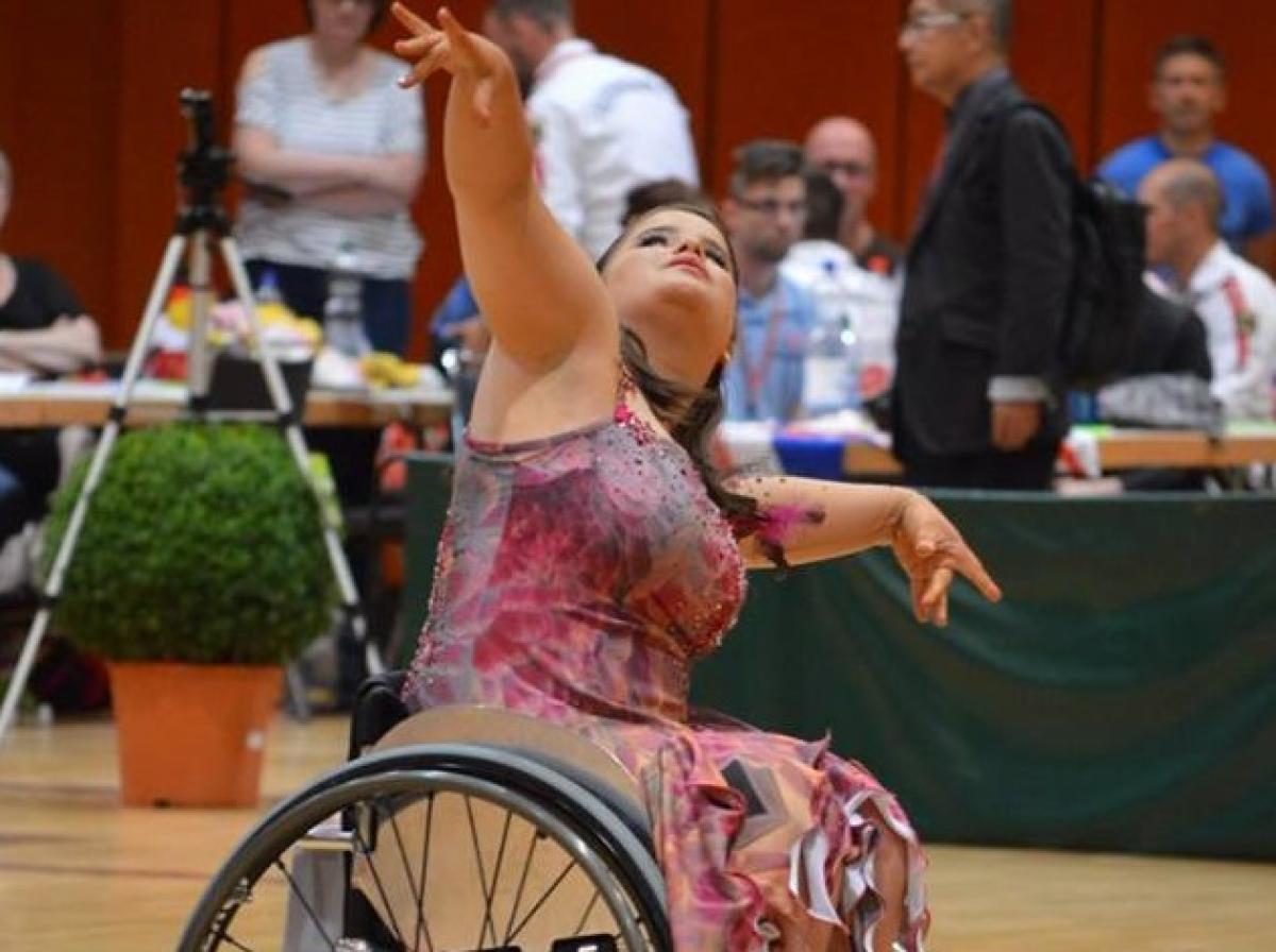 a para dancer in a wheelchair raises her arms